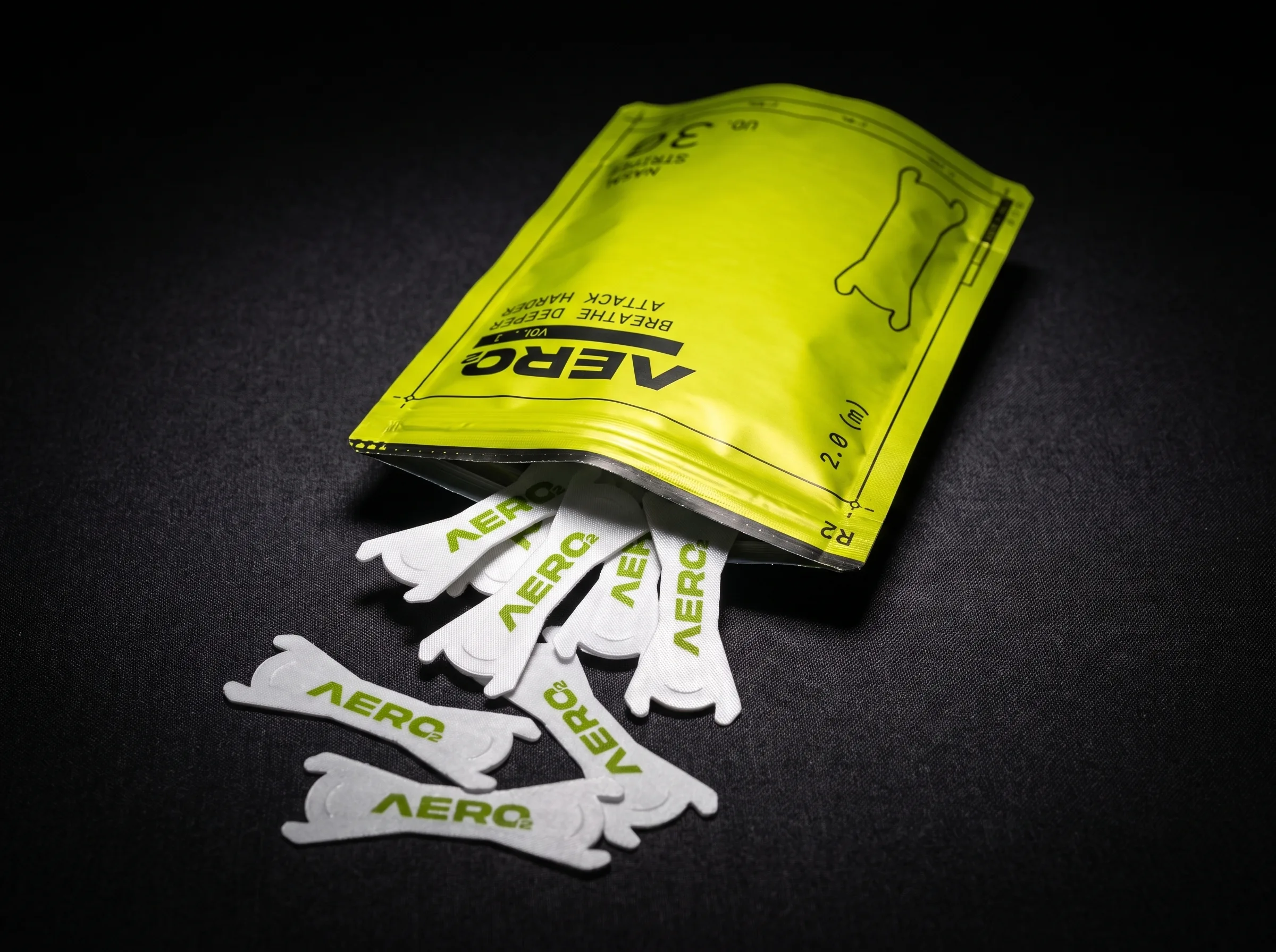 Open AERO2 pouch standing upright with several white AERO2 nasal strips spilling out onto a dark fabric surface