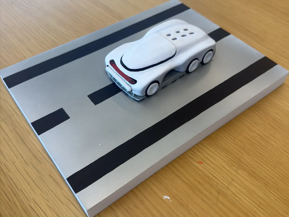 3D-printed futuristic six-wheel car prototype on a silver road-diorama plate with black lane stripes