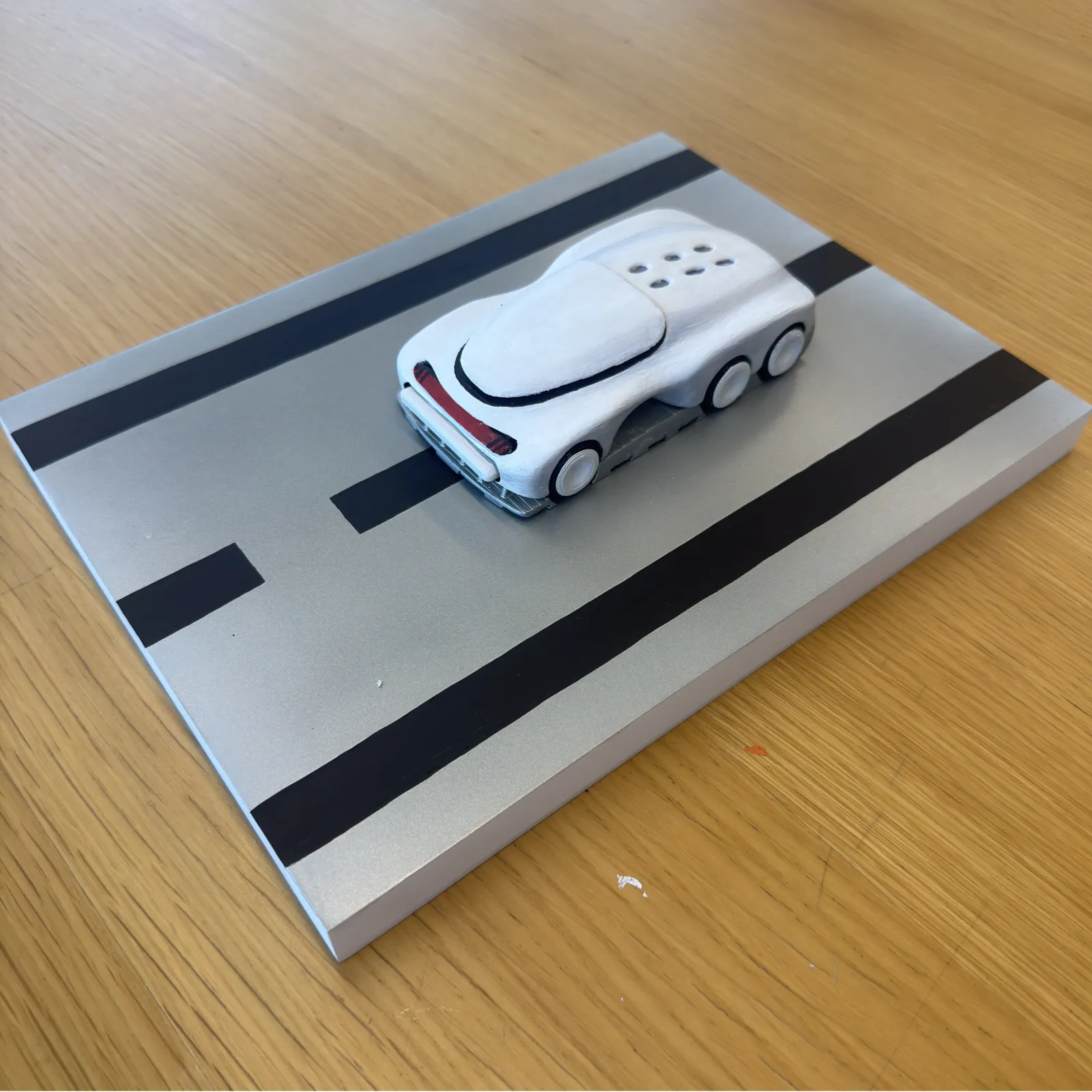 3D-printed futuristic six-wheel car prototype on a silver road-diorama plate with black lane stripes