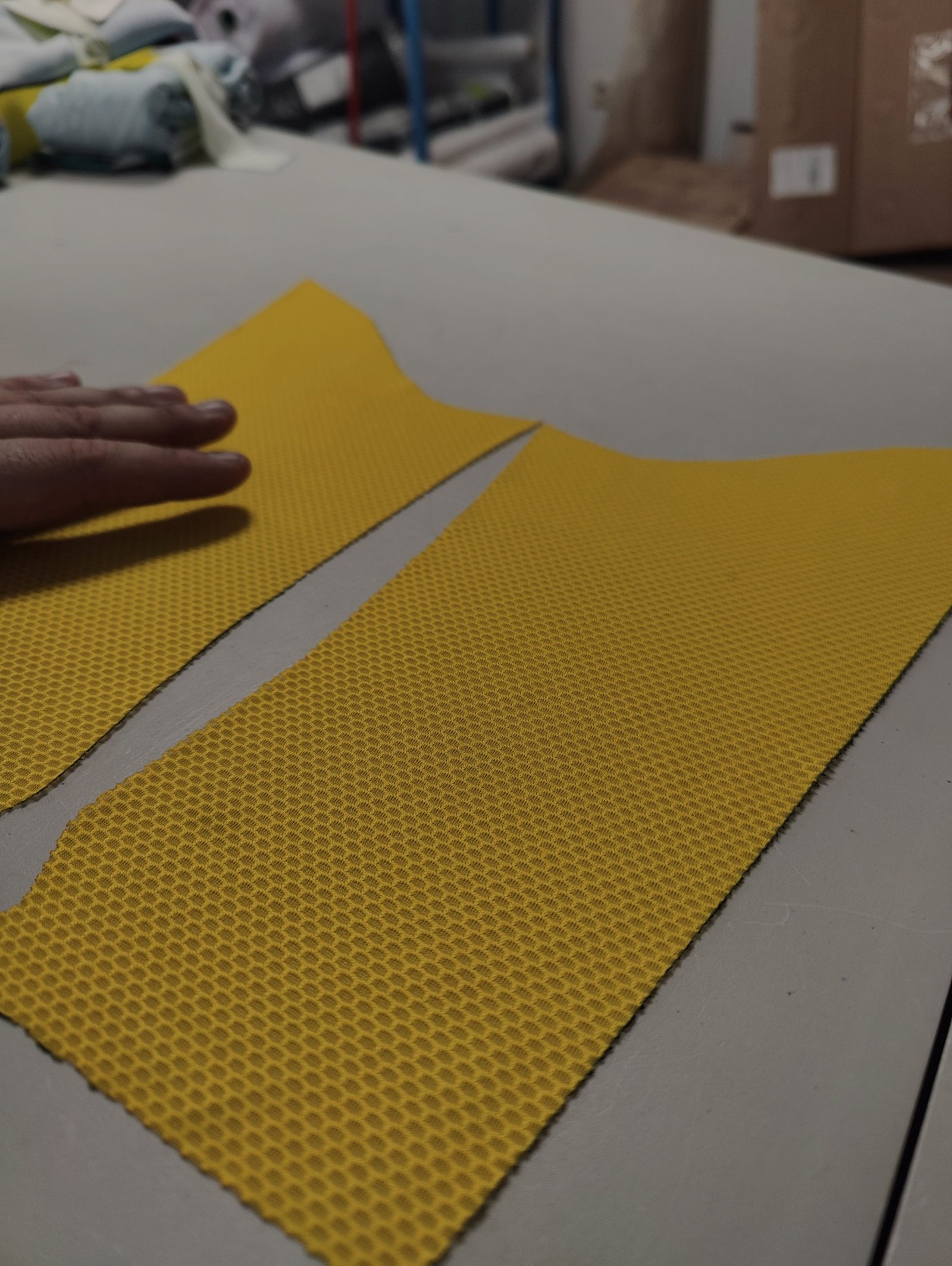 Laser-cut yellow technical fabric panels of a VELOQUE jersey pattern laid out on the workshop table