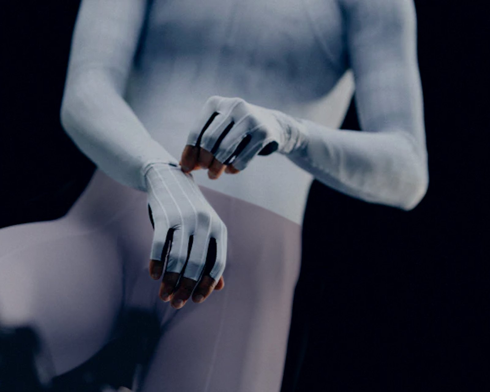 Cyclist in a VELOQUE seamless base layer adjusting a glove cuff, showing the continuous knit surface at wrist and sleeve